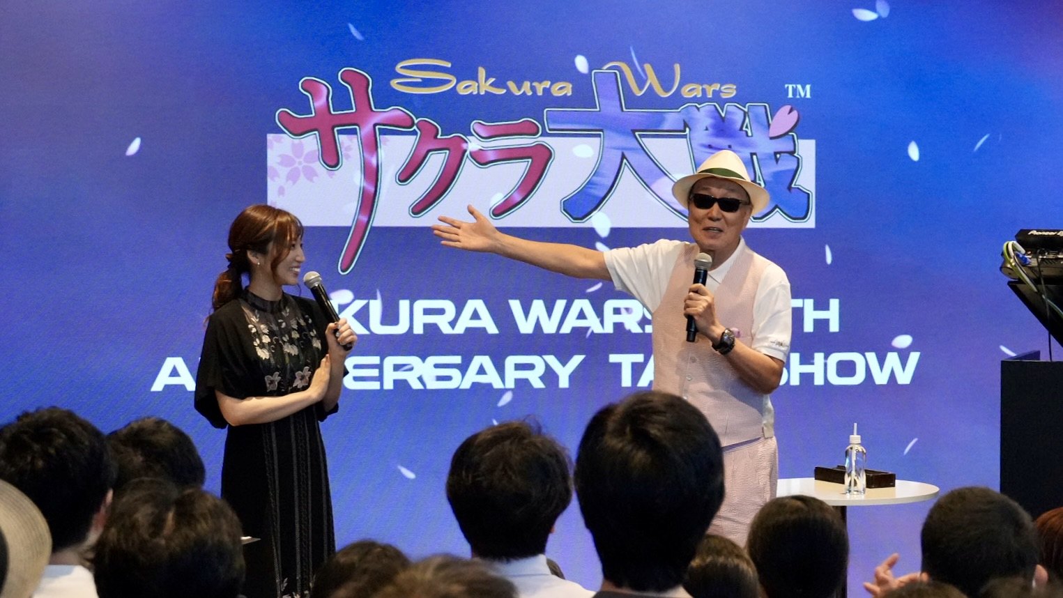 Oji Hiroi speaks toward the audience alongside the moderator at the venue of the 30th-anniversary talk show